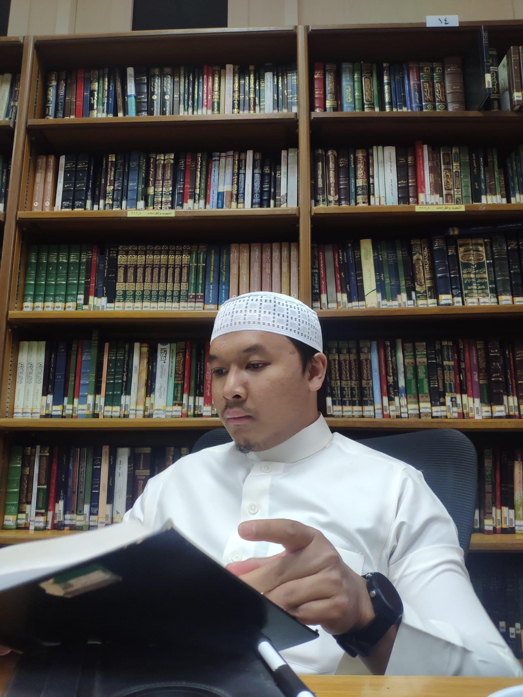 Aziz Madani sedang menuntut ilmu di ruang kajian, dikelilingi rak kitab